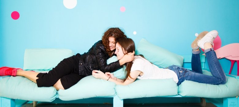 Zwei Mädchen umarmen sich und lachen gemeinsam auf dem Sofoa liegend